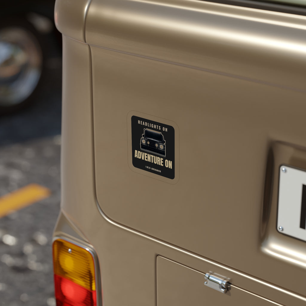 Headlights On / Adventure On die-cut sticker: a head-on 4x4 with glowing headlights between HEADLIGHTS ON and ADVENTURE ON lettering on black – view 4